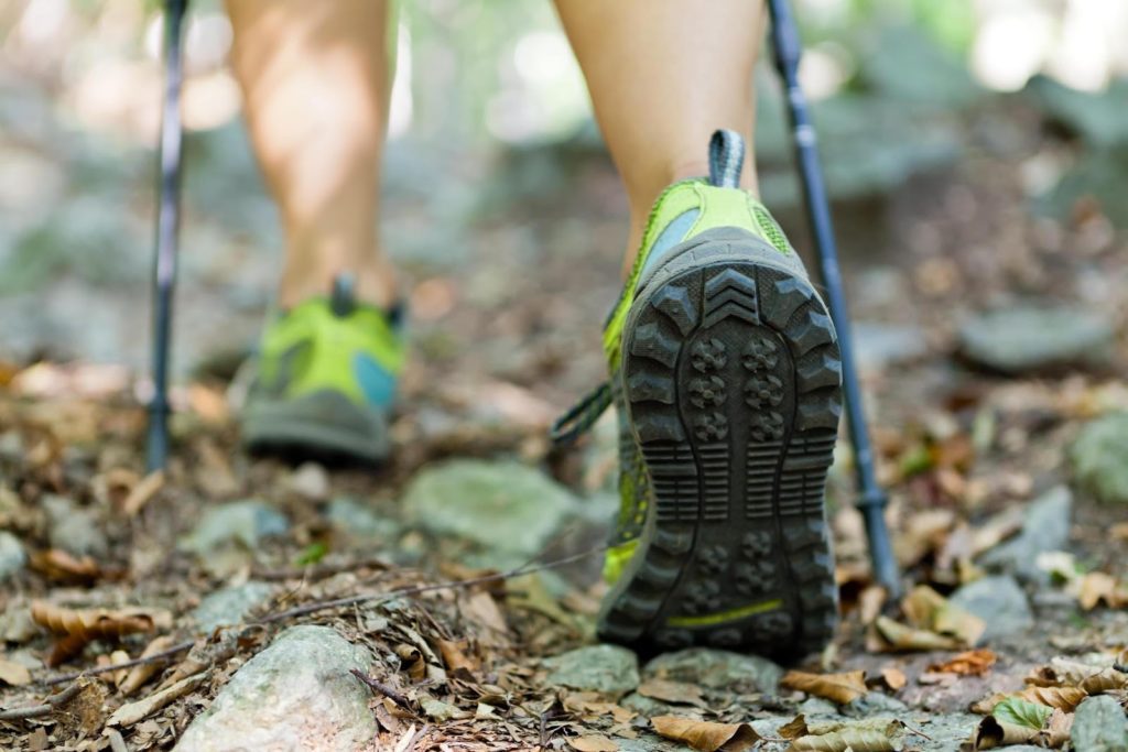 Nohy v turistickej obuvi a palice na nordic walking na lesnom chodníku
